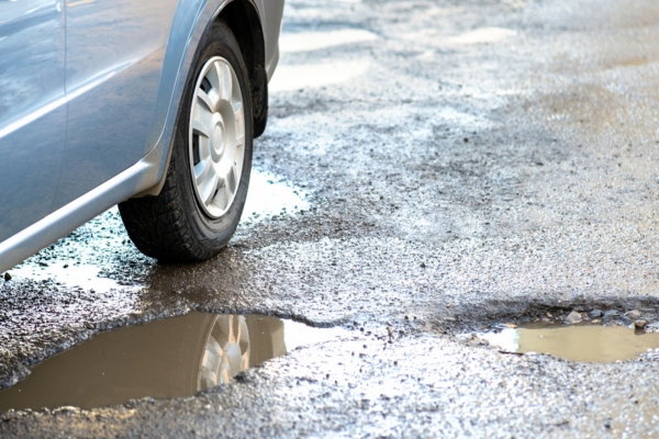 image of car wheel driving on wet rough road with potholes