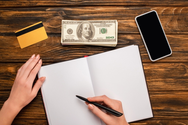 woman about to write on a blank notebook with credit card and cash in front depicting auto glass replacement cost