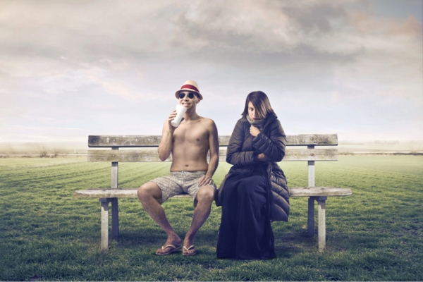woman in full winter wear and man in summer outfit both sitting on a bench depicting temperature changes