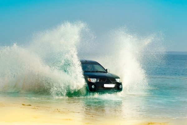 car speeding on shallow water by the beach that may cause windshield pitting