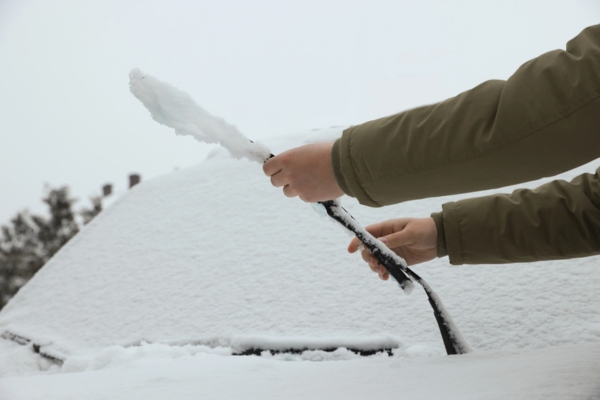 Woman cleaning car wiper blade covered with snow outdoors