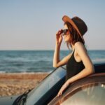 woman looking at the beach beside her parked car in the summer