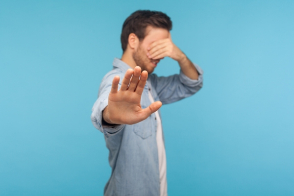 man covering eyes with one hand and another hand extended making a stop sign depicting ignoring auto glass damage