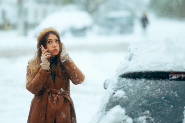 woman on the phone while stuck in snow with a broken car glass