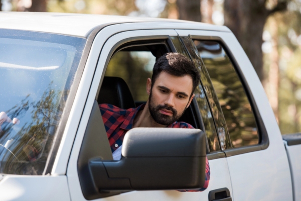 man looking at the side mirror of his truck