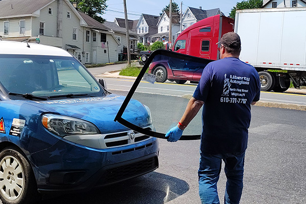 Ebervale, PA technician carrying a new windshield for replacement on a vehicle